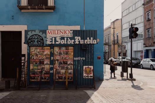 Street view of a newsstand in vibrant Puebla, Mexico with urban architecture and pedestrians.