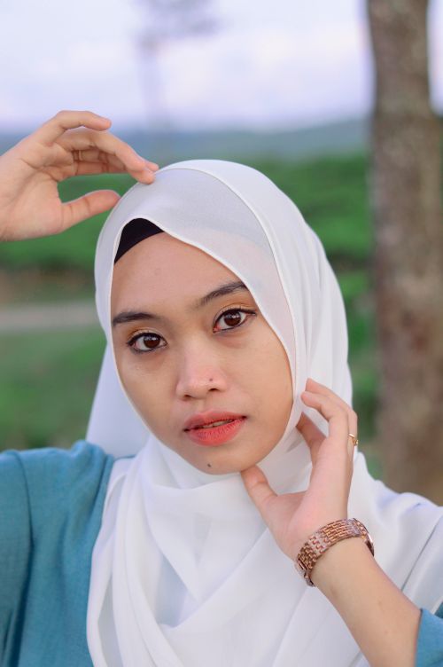 Free Beautiful close-up portrait of a woman wearing a white hijab and wristwatch in an outdoor setting. Stock Photo