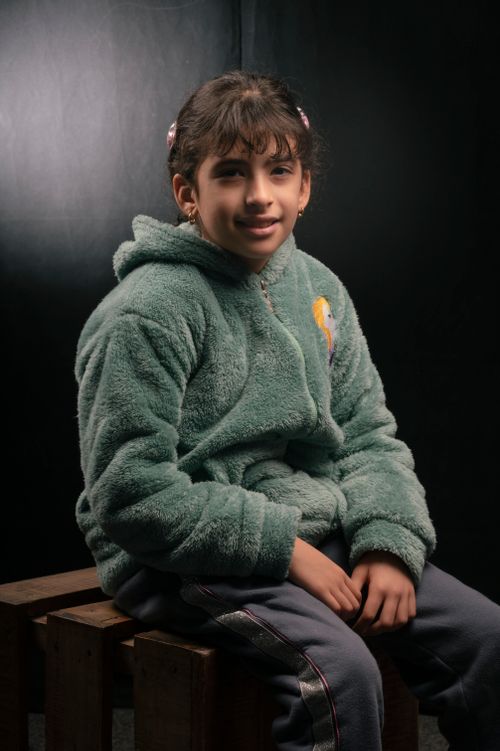 Free Studio portrait of a smiling girl in a green fluffy jacket sitting on wooden boxes. Stock Photo