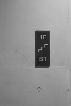 Black and white image of a minimalist concrete wall featuring a directional sign for floors 1F and B1.