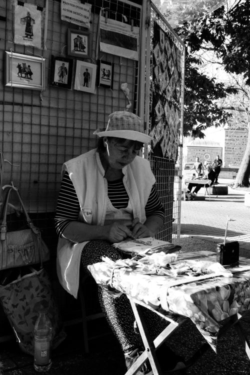 Free Black and white photo of an elderly woman selling her artwork at a bustling city street market. Stock Photo