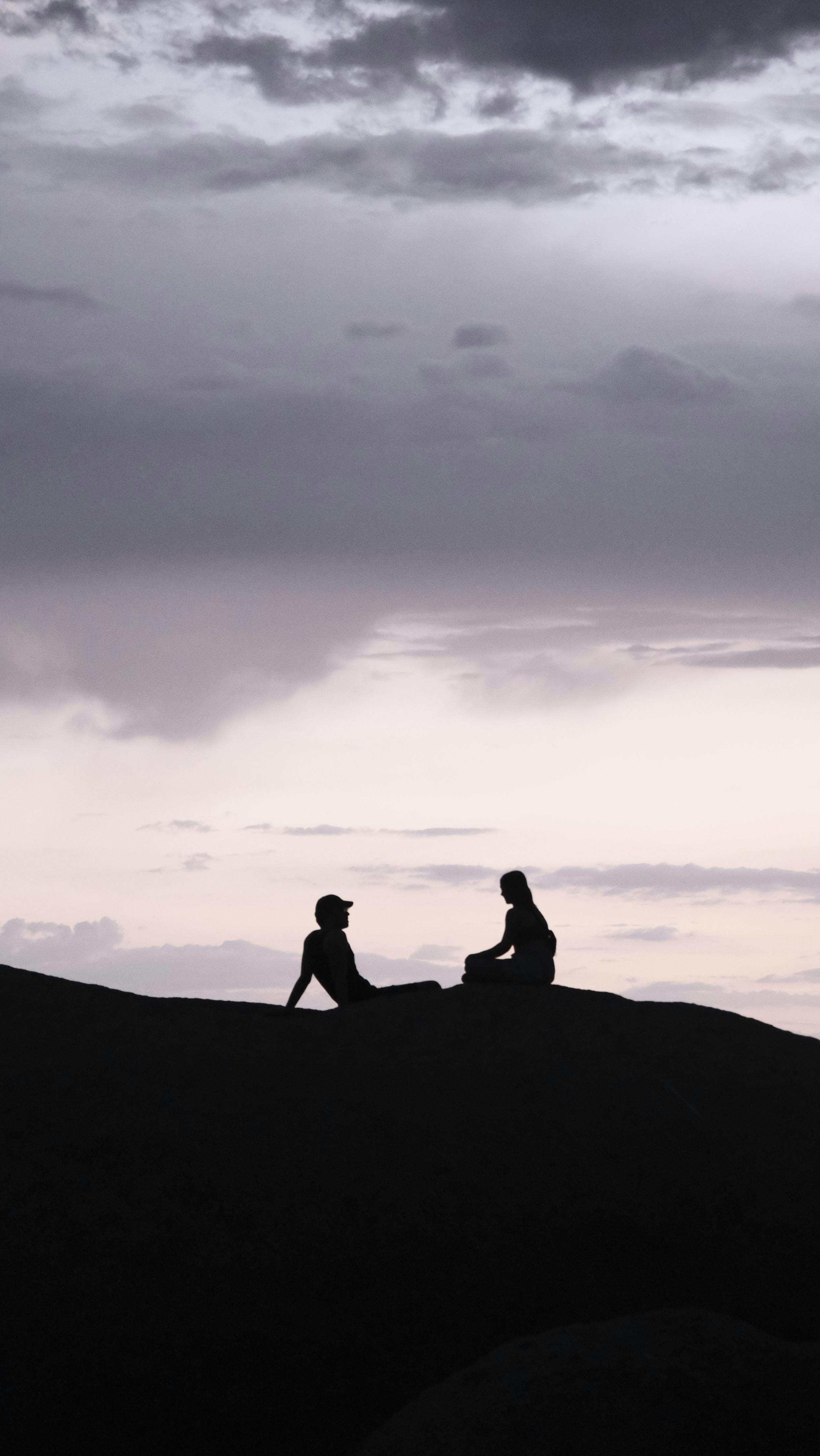 A man and a woman silhouetted against a vibrant sunset sky atop a hill, captured in a serene moment.
