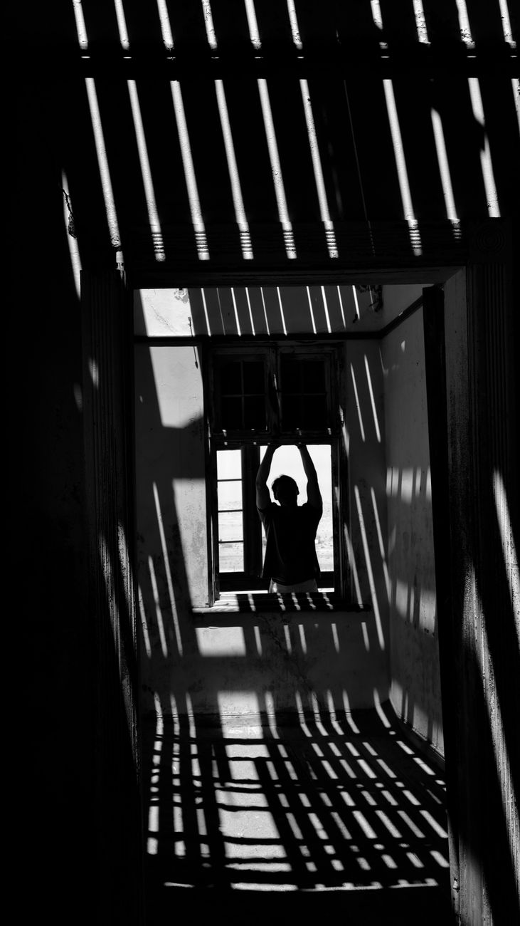 Black and white silhouette of a person in dramatic light through window patterns.. black, white, silhouette