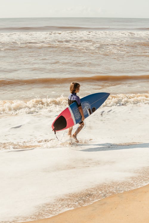 A Child Walking on the Beach with a Surfboard 