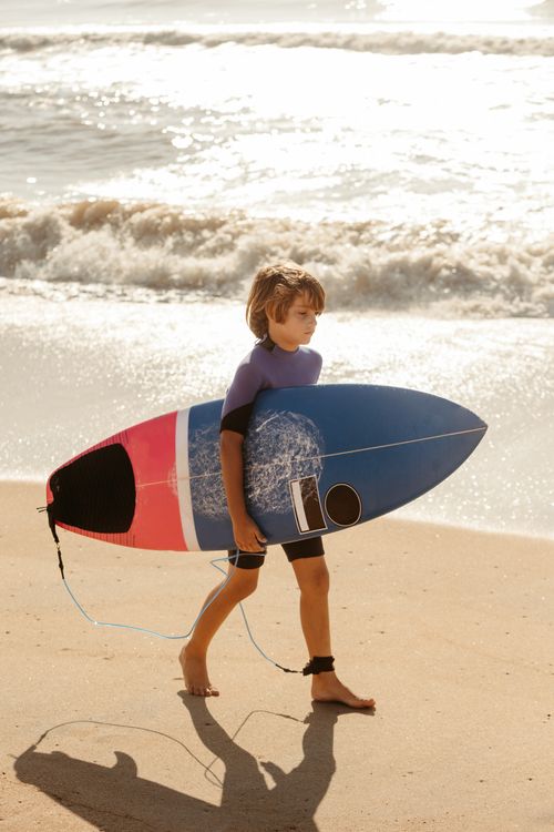 Free A young boy carries a colorful surfboard along a sandy beach on a sunny day. Stock Photo