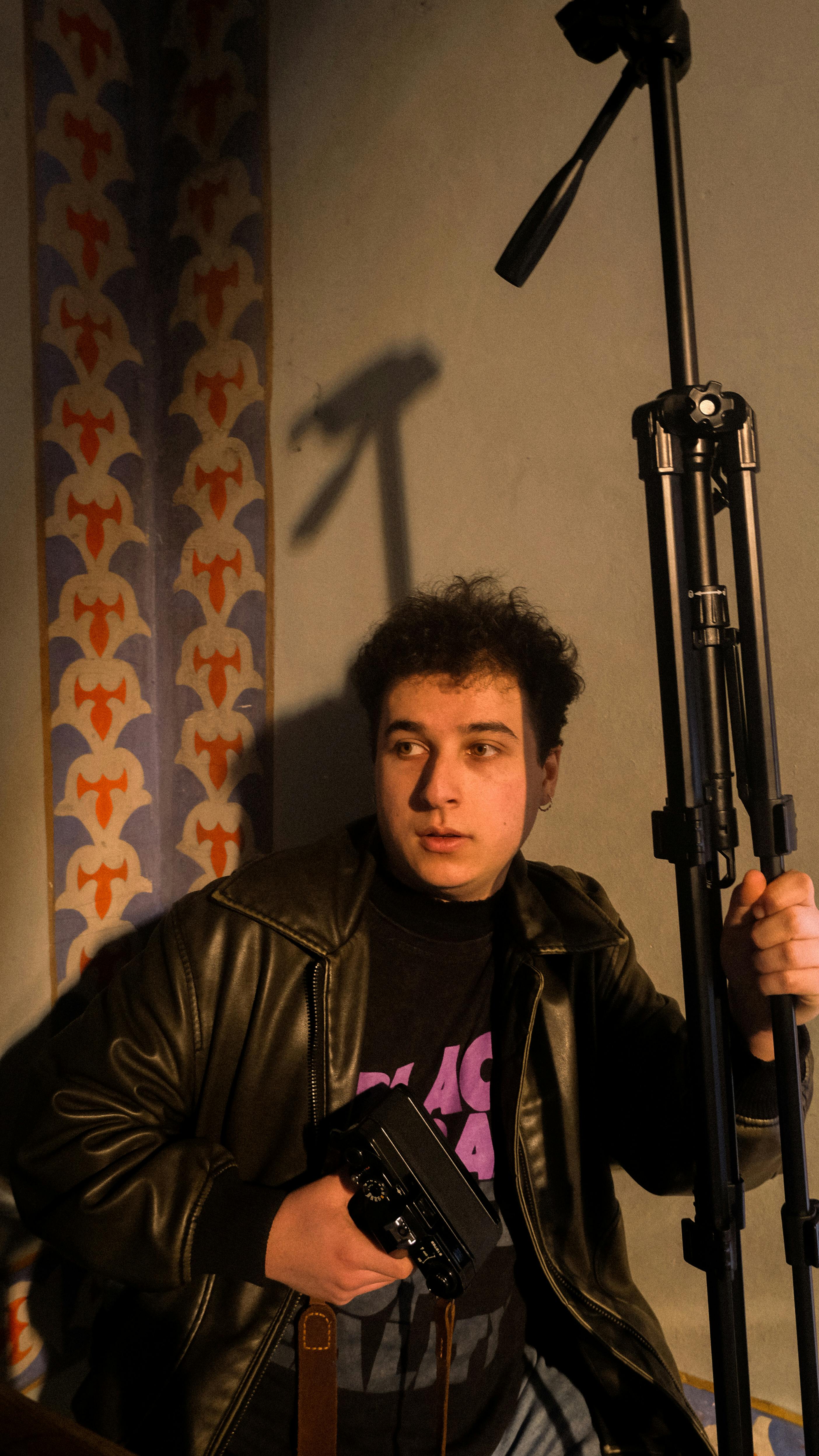 Moody indoor portrait of a person with a camera and tripod, emphasizing the art of photography.