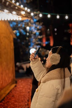 Woman capturing festive lights on a winter night with her smartphone.