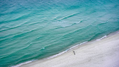 Free A stunning aerial shot capturing an empty beach beside the emerald ocean waves under a clear sky. Stock Photo