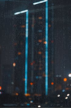 A rainy night view of Jakarta's skyline with skyscrapers and blurred city lights.