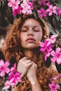 一位闭着眼睛的卷发女人，神态宁静，周身环绕着鲜艳的粉红色花朵