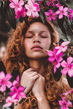 一位闭着眼睛的卷发女人，神态宁静，周身环绕着鲜艳的粉红色花朵