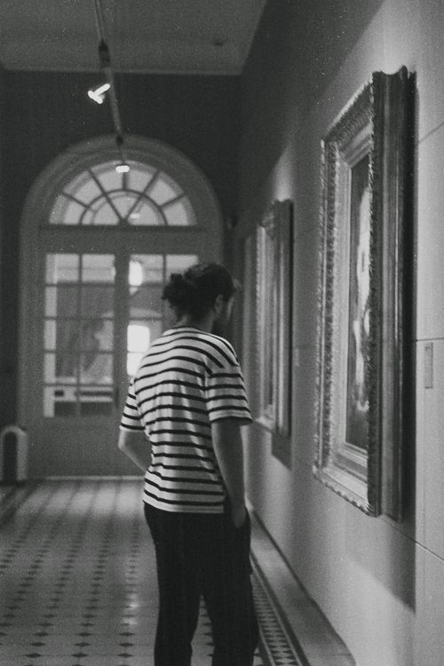 Free A person in a striped shirt admires paintings in a museum hallway. Black and white photography. Stock Photo
