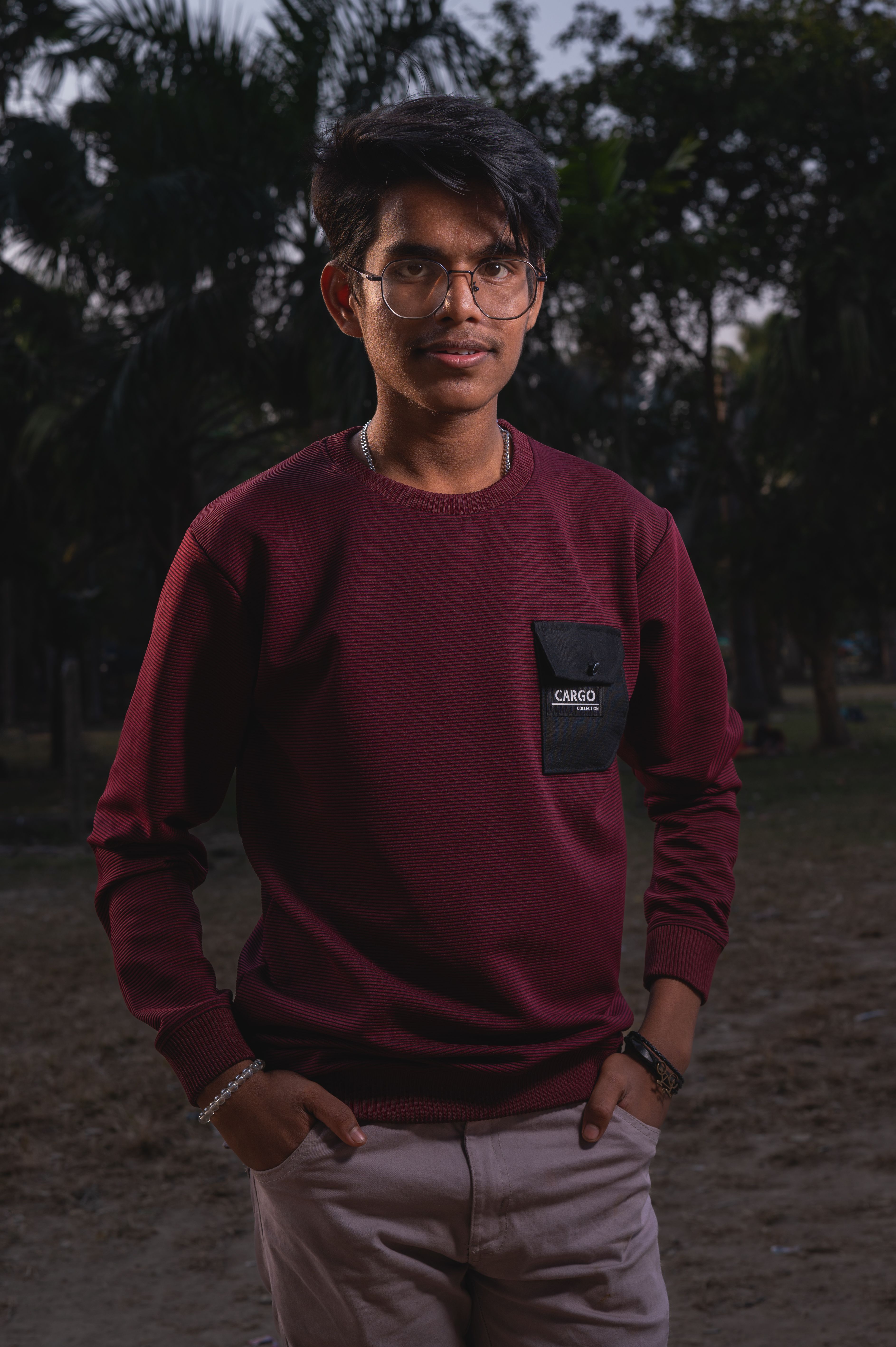 Portrait of a young man in a burgundy sweatshirt standing outdoors during the day.