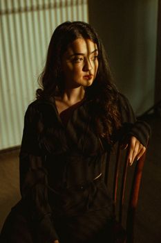 Fashion portrait of a woman in a black outfit, illuminated by shadowed sunlight indoors.