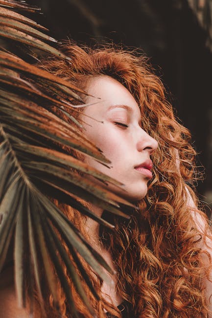 A peaceful portrait of a woman with curly hair and closed eyes, set against a natural backdrop.