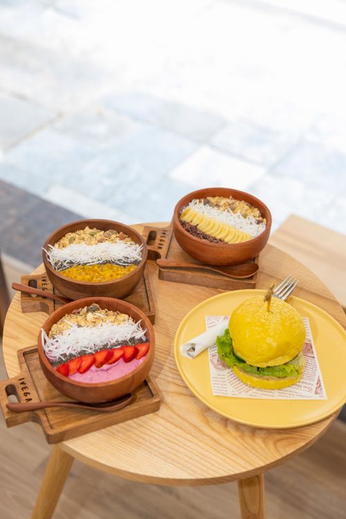 Free Wooden bowls with breakfast foods on a table next to a vibrant yellow burger. Stock Photo