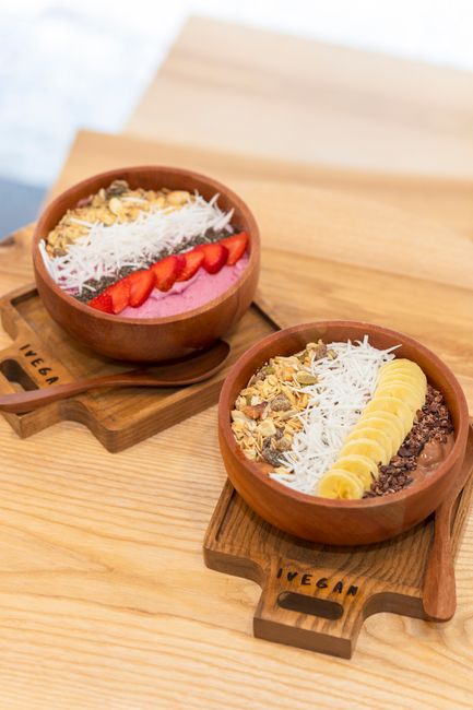 Two delicious vegan smoothie bowls topped with fruits on wooden trays, perfect for a healthy breakfast.