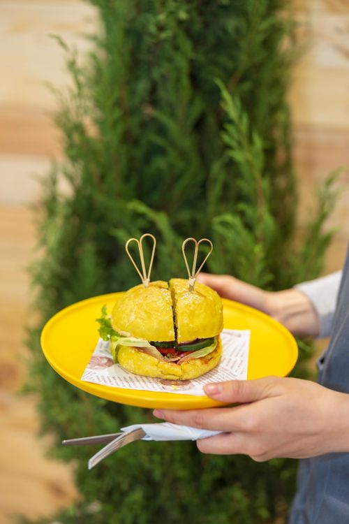 Free Close-up of a delicious vegan burger with vegetable filling on a vibrant yellow plate, perfect for foodie inspiration. Stock Photo