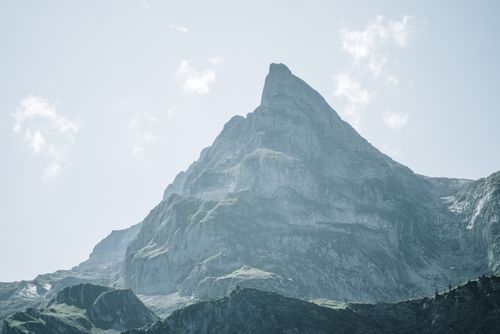 Free A dramatic view of a towering rocky mountain peak shrouded in mist and clouds in daylight. Stock Photo