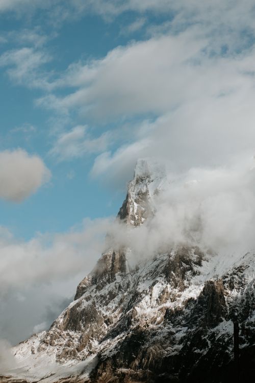 Free A breathtaking view of a snow-capped mountain peak partially covered by clouds, reaching into a clear blue sky. Stock Photo