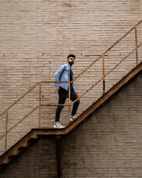 Free Man in denim shirt walking up outdoor staircase against brick wall. Stock Photo