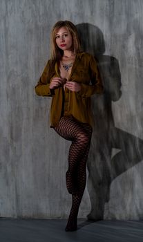 Model posing against textured wall wearing blouse and stockings in a modern fashion photo.
