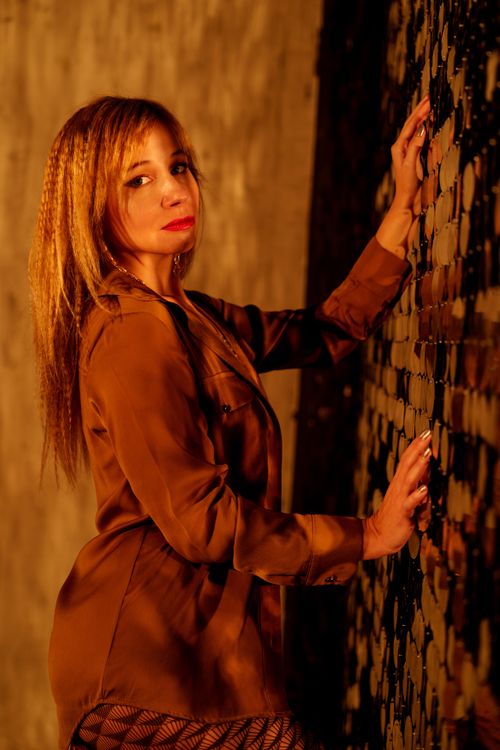 Free A stylish woman poses confidently against a textured mosaic wall in warm lighting. Stock Photo