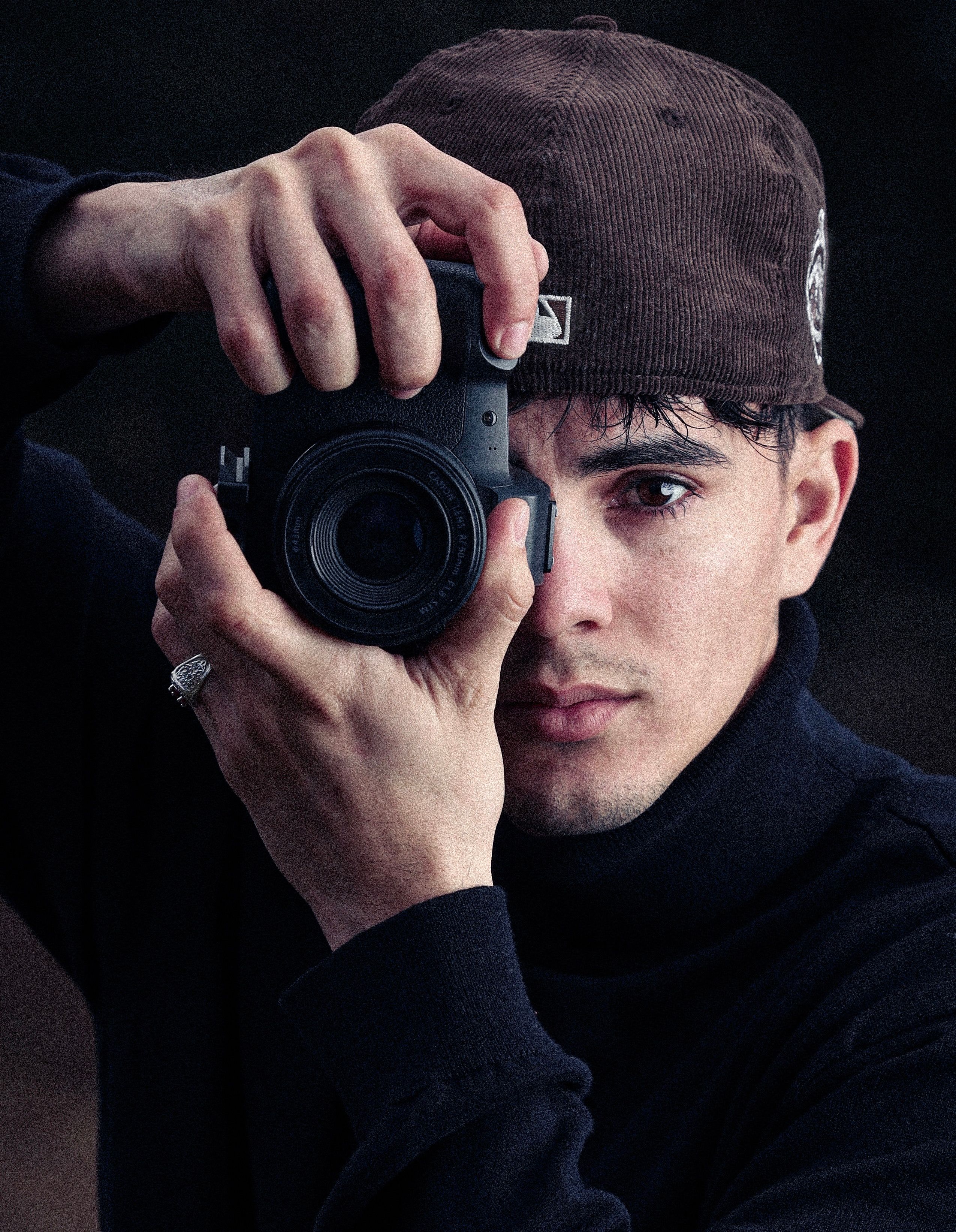 A young man in Oklahoma City focuses through his camera lens, wearing a hat and capturing the perfect shot.