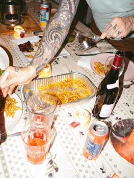 Close-up of a casual dinner setting with drinks, food, and tattooed hands in Montréal.