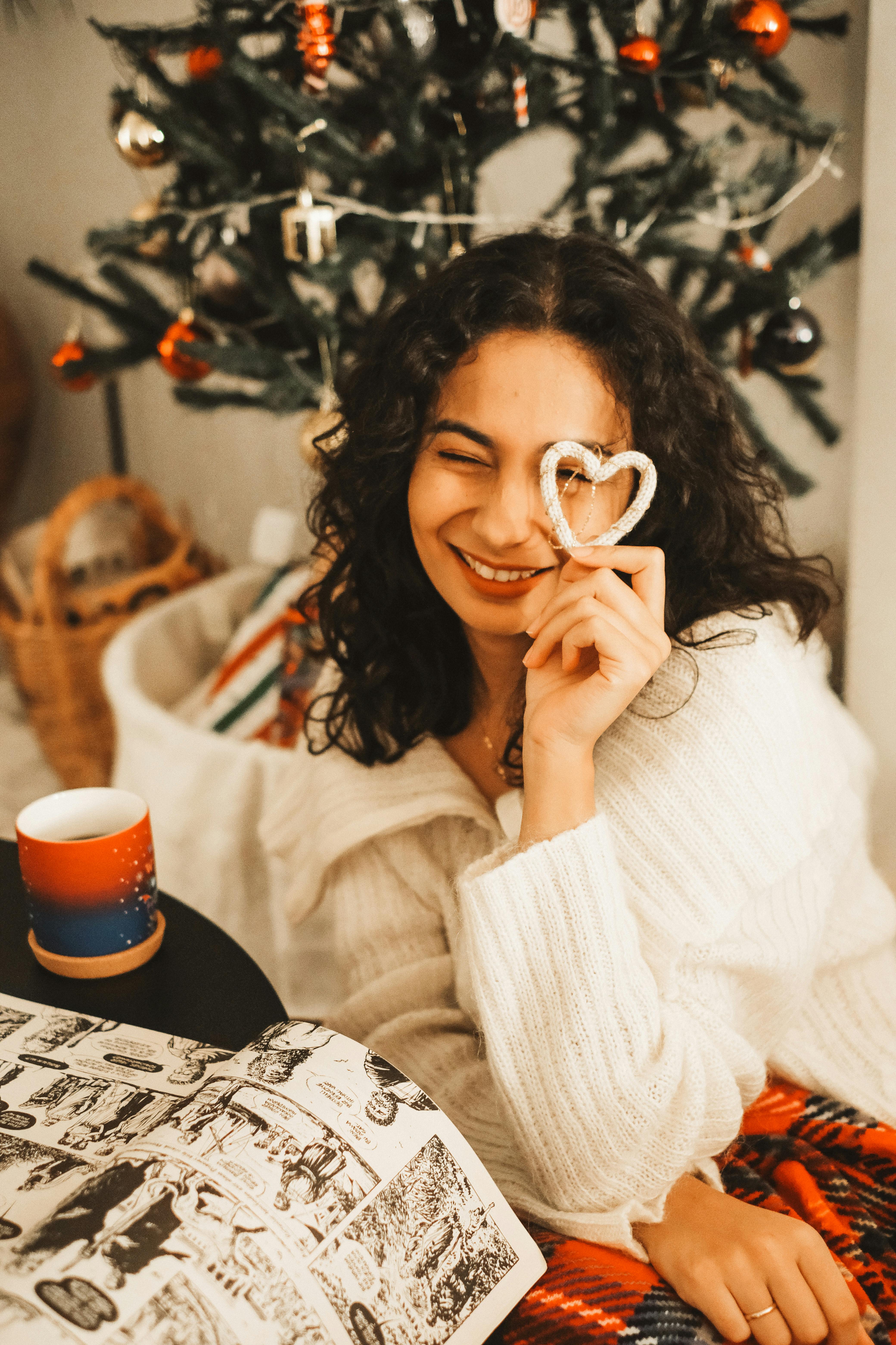 woman reading a comic book sitting by the christmas tree looking through an ornament