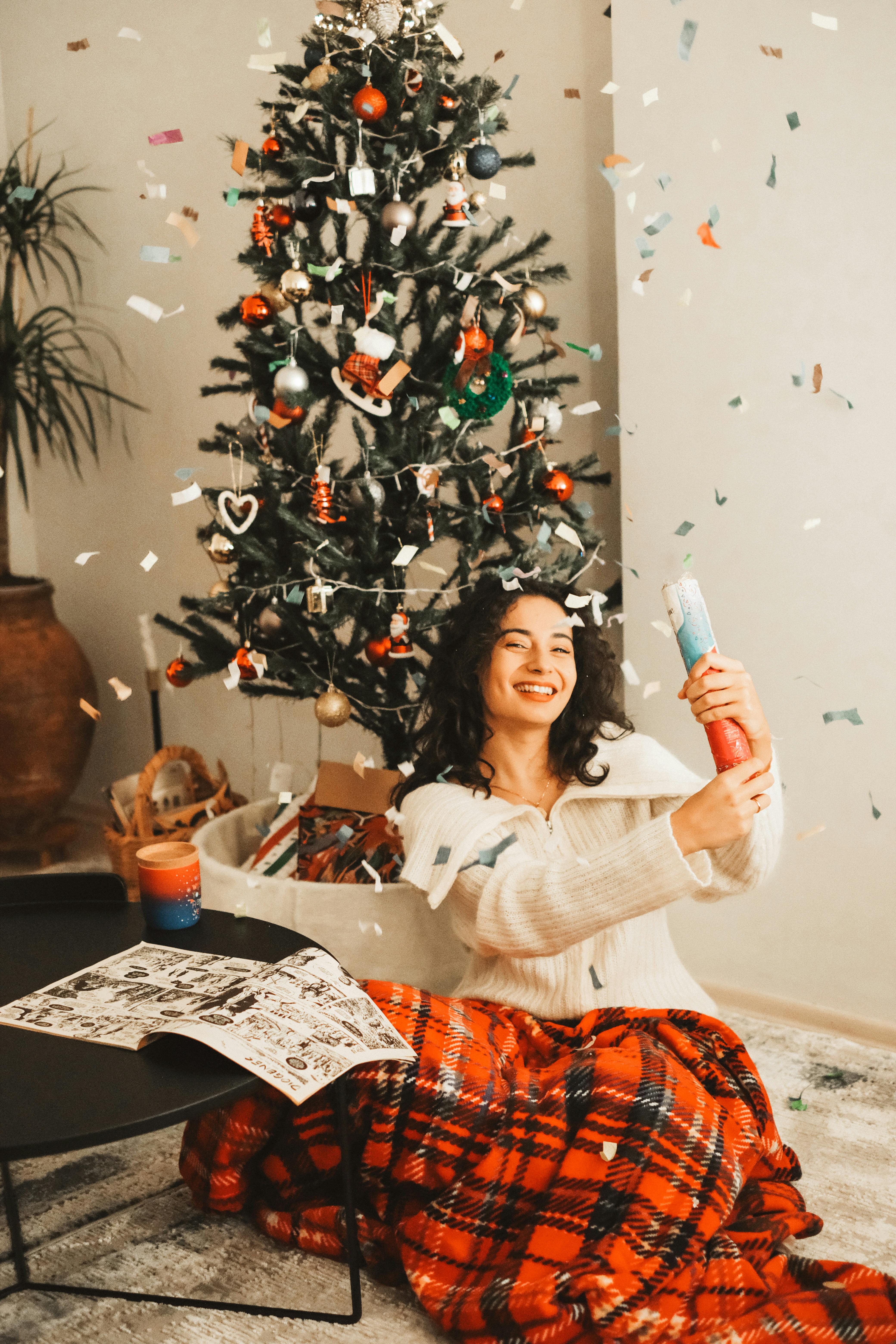 smiling woman shooting confetti cannon sitting in the living room by the christmas tree