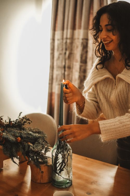 Free A woman lights a candle in a cozy winter setting, creating a warm, festive atmosphere. Stock Photo