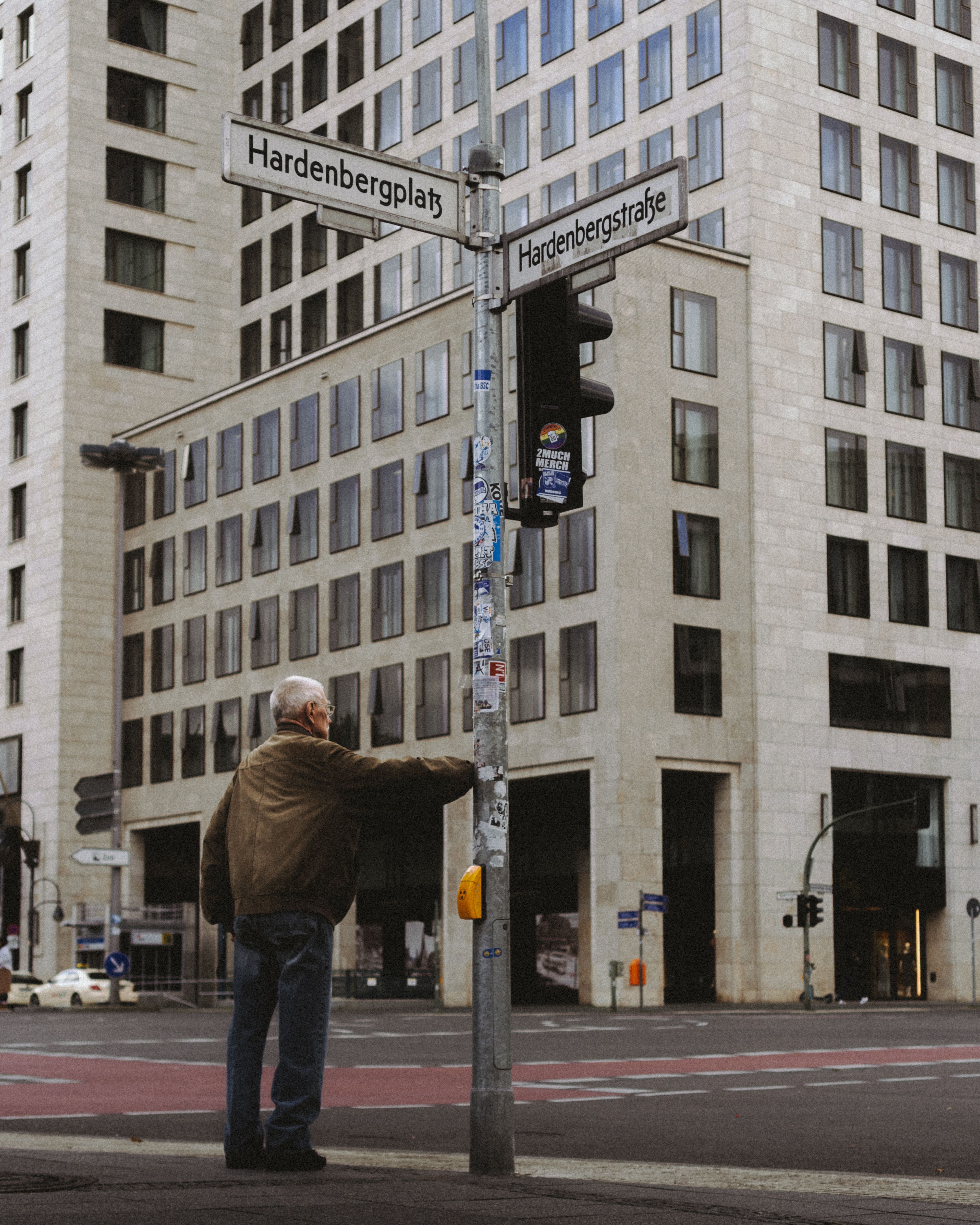 An elderly man waits at a crosswalk in Berlin's urban environment.