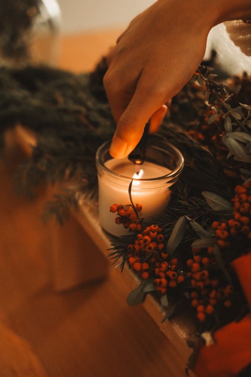 Free Hand lighting a candle surrounded by festive Christmas decorations, creating a warm atmosphere. Stock Photo