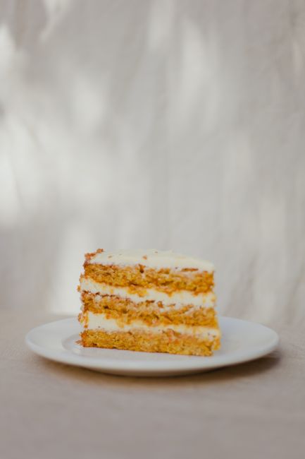 Delicious slice of homemade carrot cake with cream cheese frosting on a white plate.