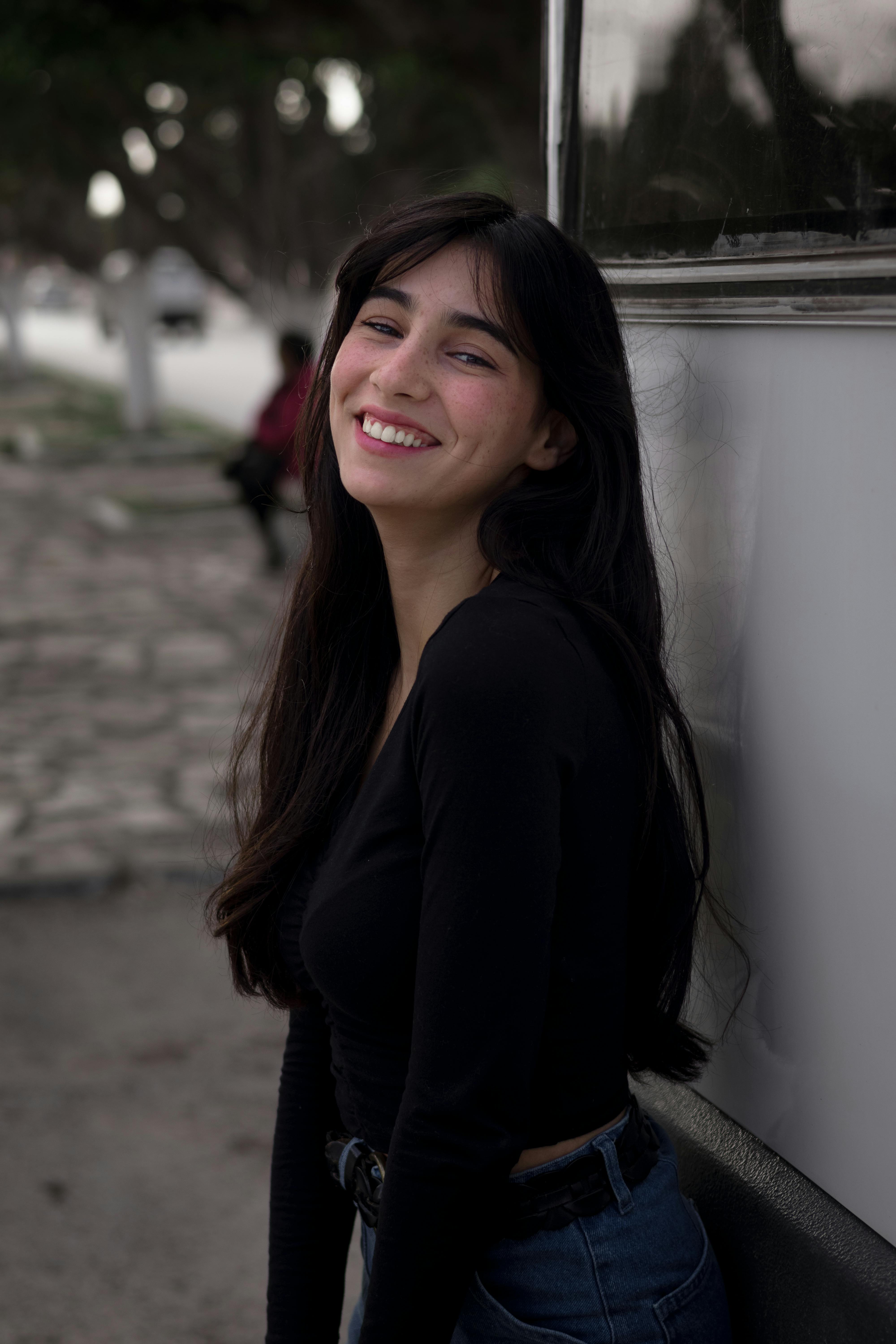 Portrait of a smiling young woman with long hair posing outdoors in casual attire.