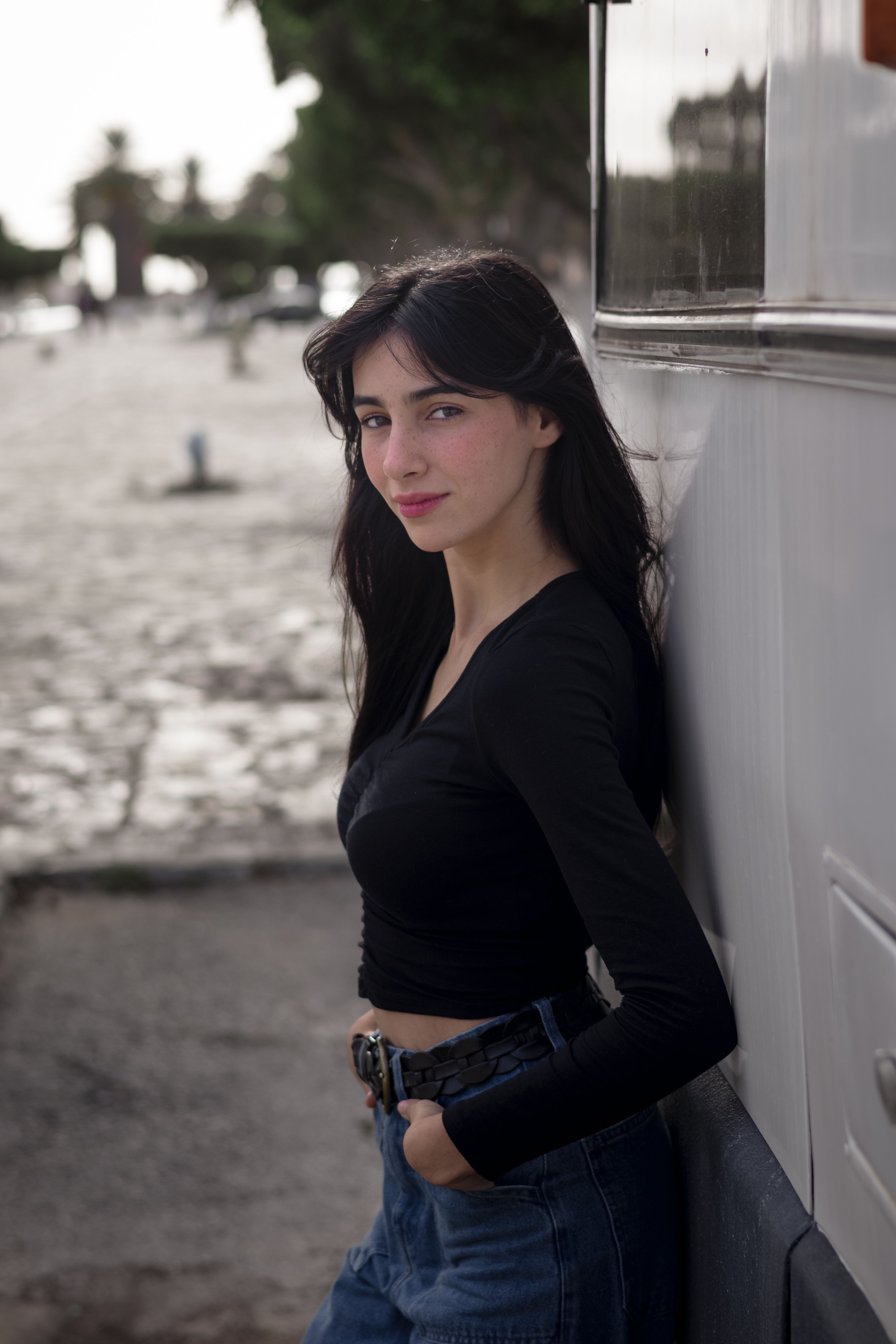 Black-haired woman in a black crop top and jeans poses outdoors, exuding modern street style.