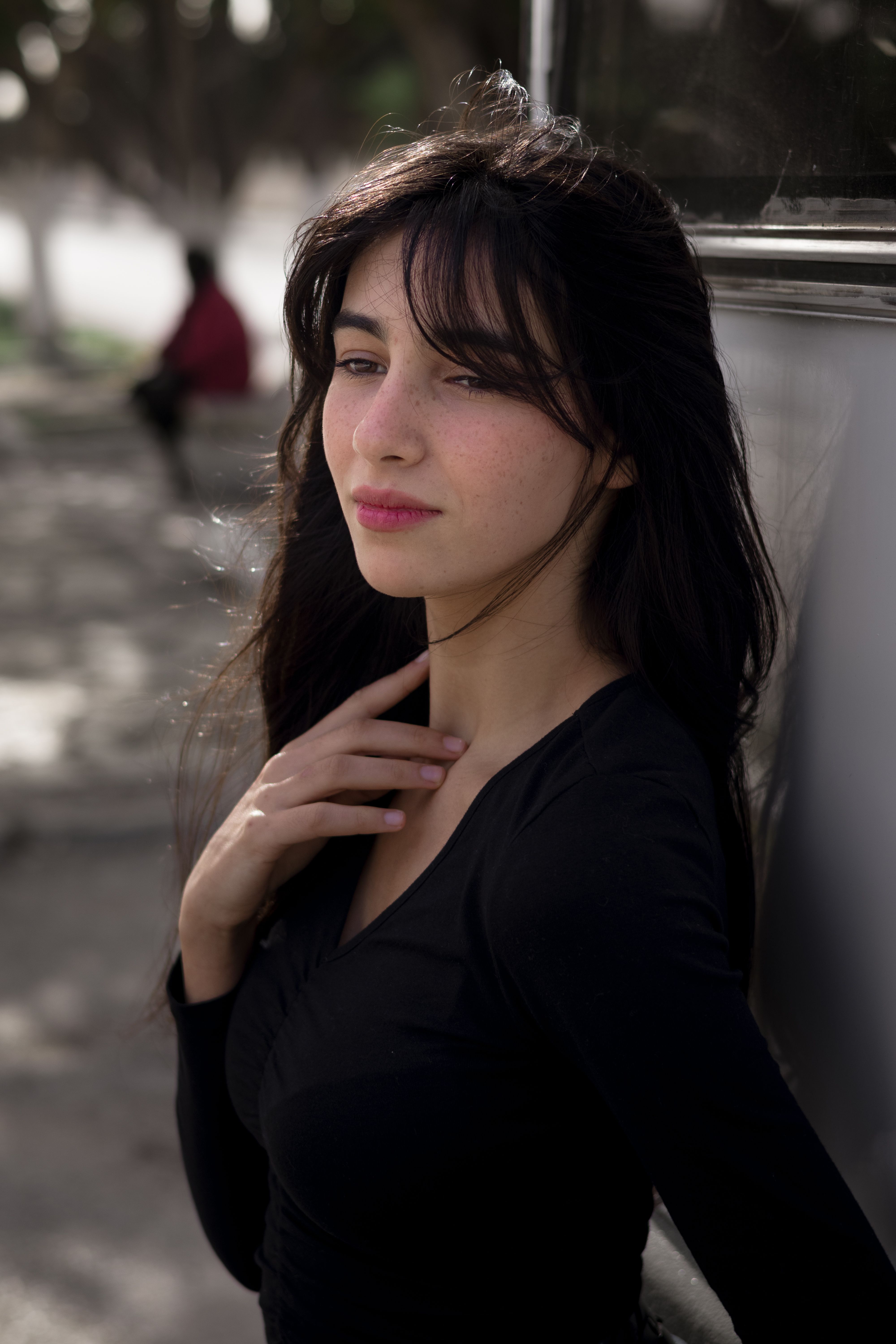 Stylish woman in black top posing outdoors with long black hair and a thoughtful expression.