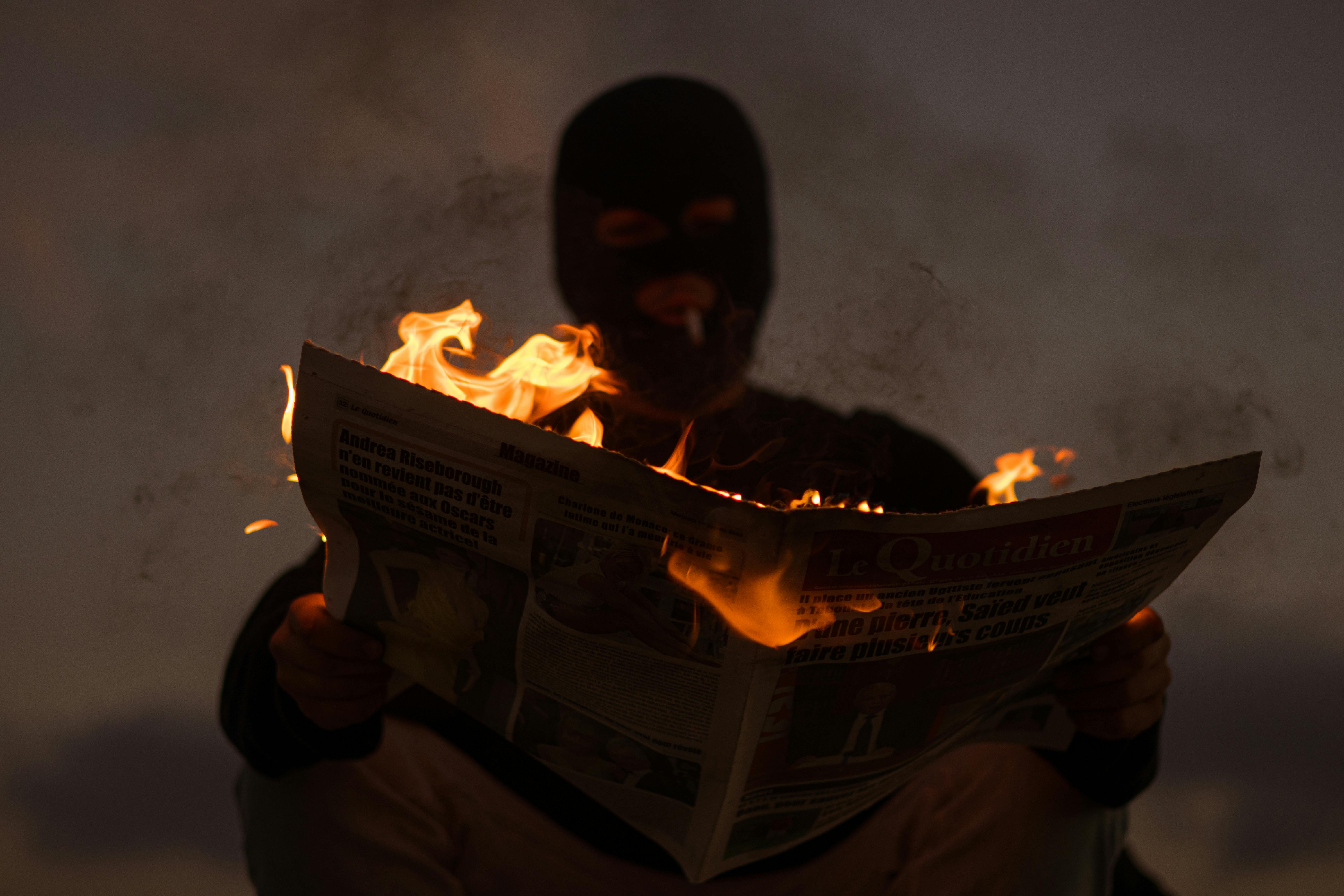 masked man reading burning newspaper