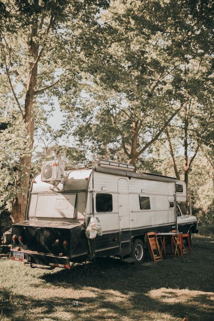 A parked rental RV at a quiet forest campsite with morning light