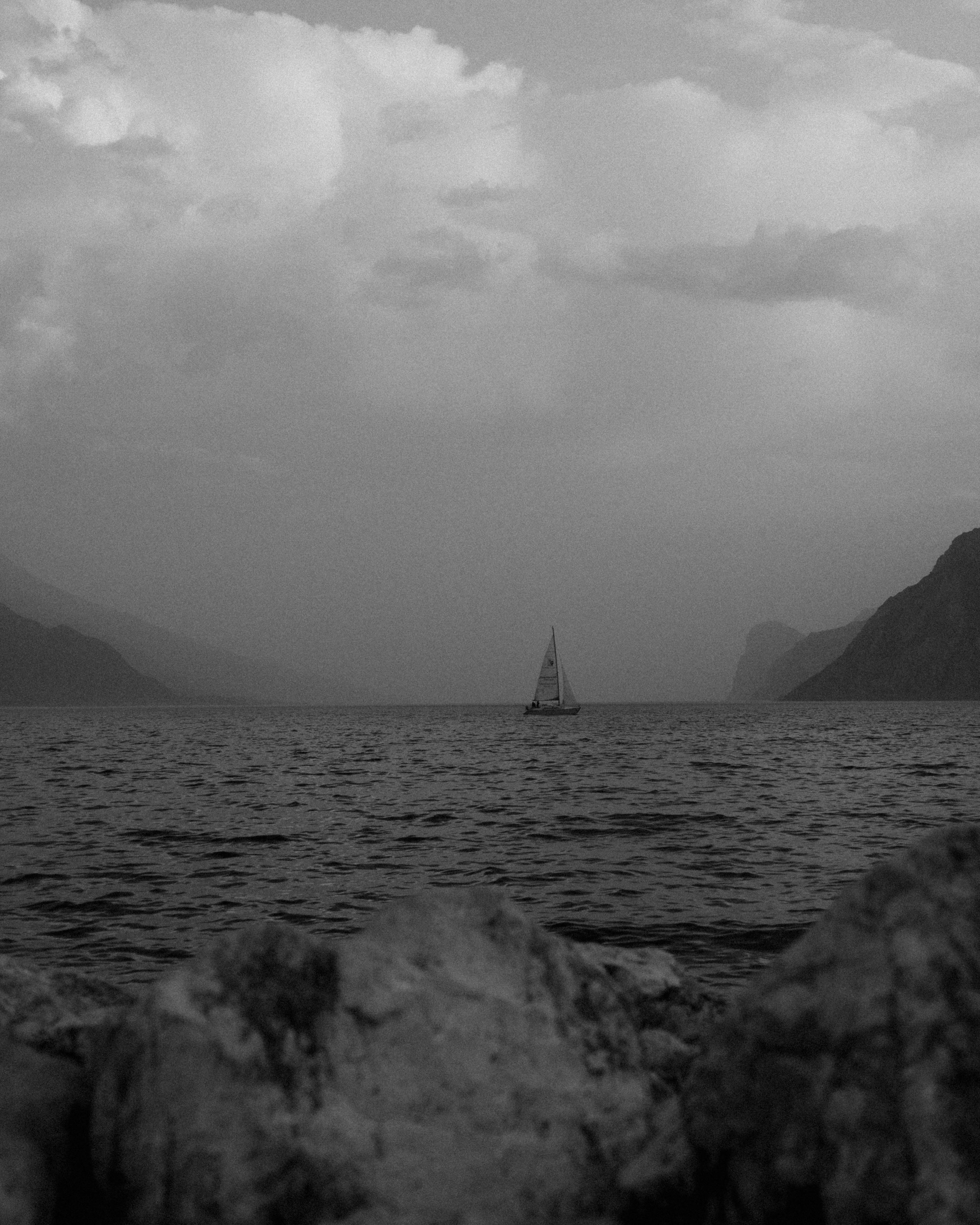 Sailboat on Lake Garda with mountains in the background, captured on an overcast day.