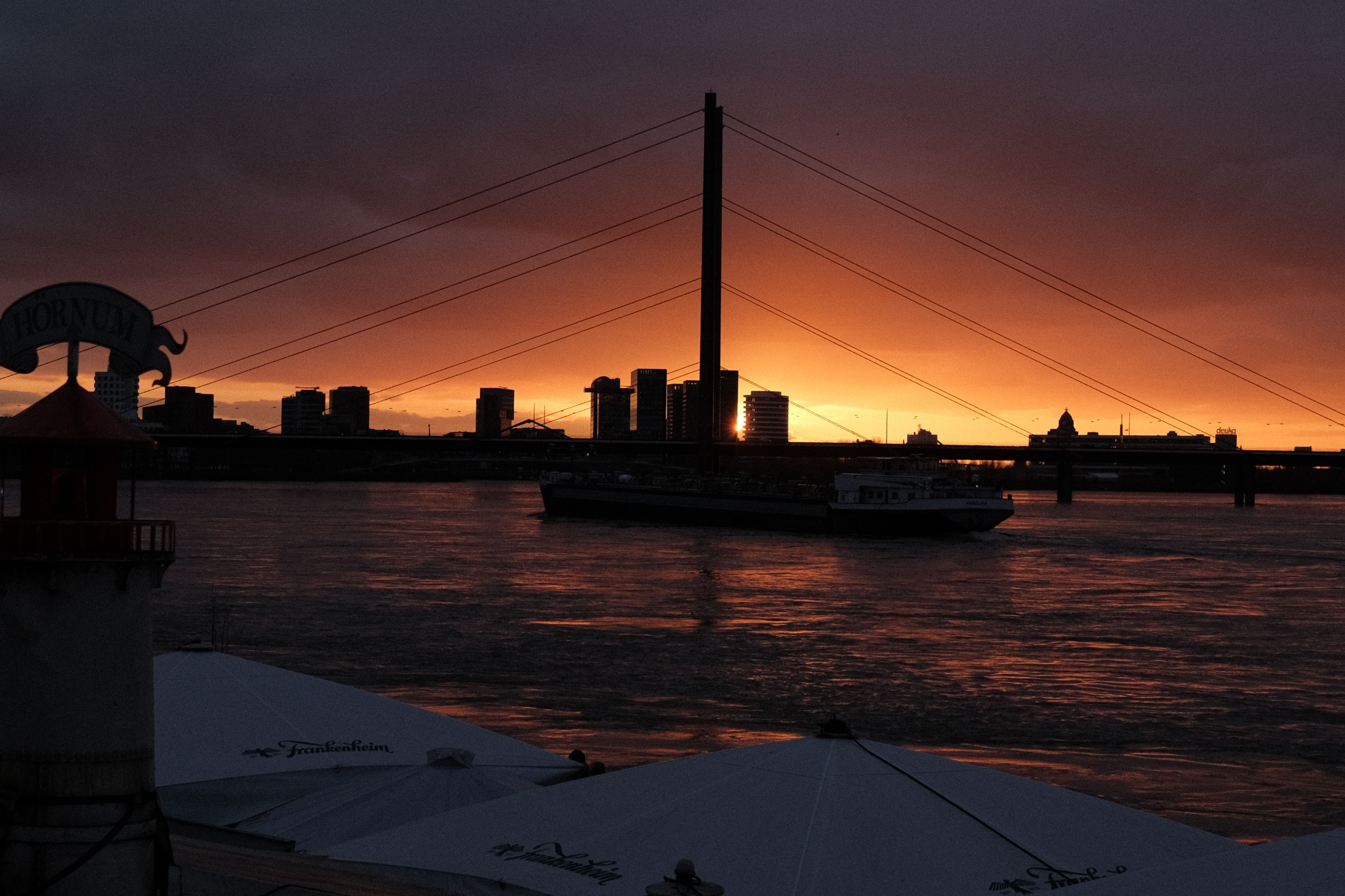 Dramatic sunset view over the Rhine River in Düsseldorf with city skyline and bridge silhouette.