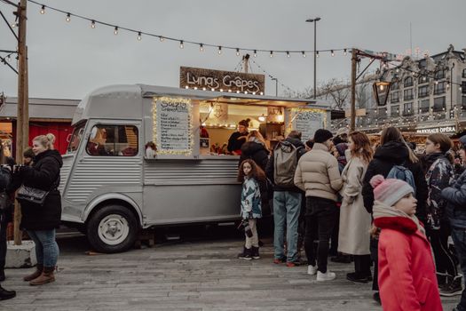People gather at a cozy Christmas market in Zürich, enjoying crepes from a vintage food truck adorned with lights.