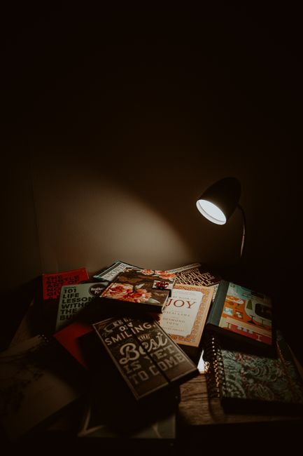 A warm, dimly-lit reading corner featuring a tabletop lamp illuminating a collection of books. A warm, dimly-lit reading corner featuring a tabletop lamp illuminating a collection of books.