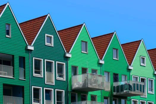 Vibrant green houses with balconies against a blue sky in Zaanstad.