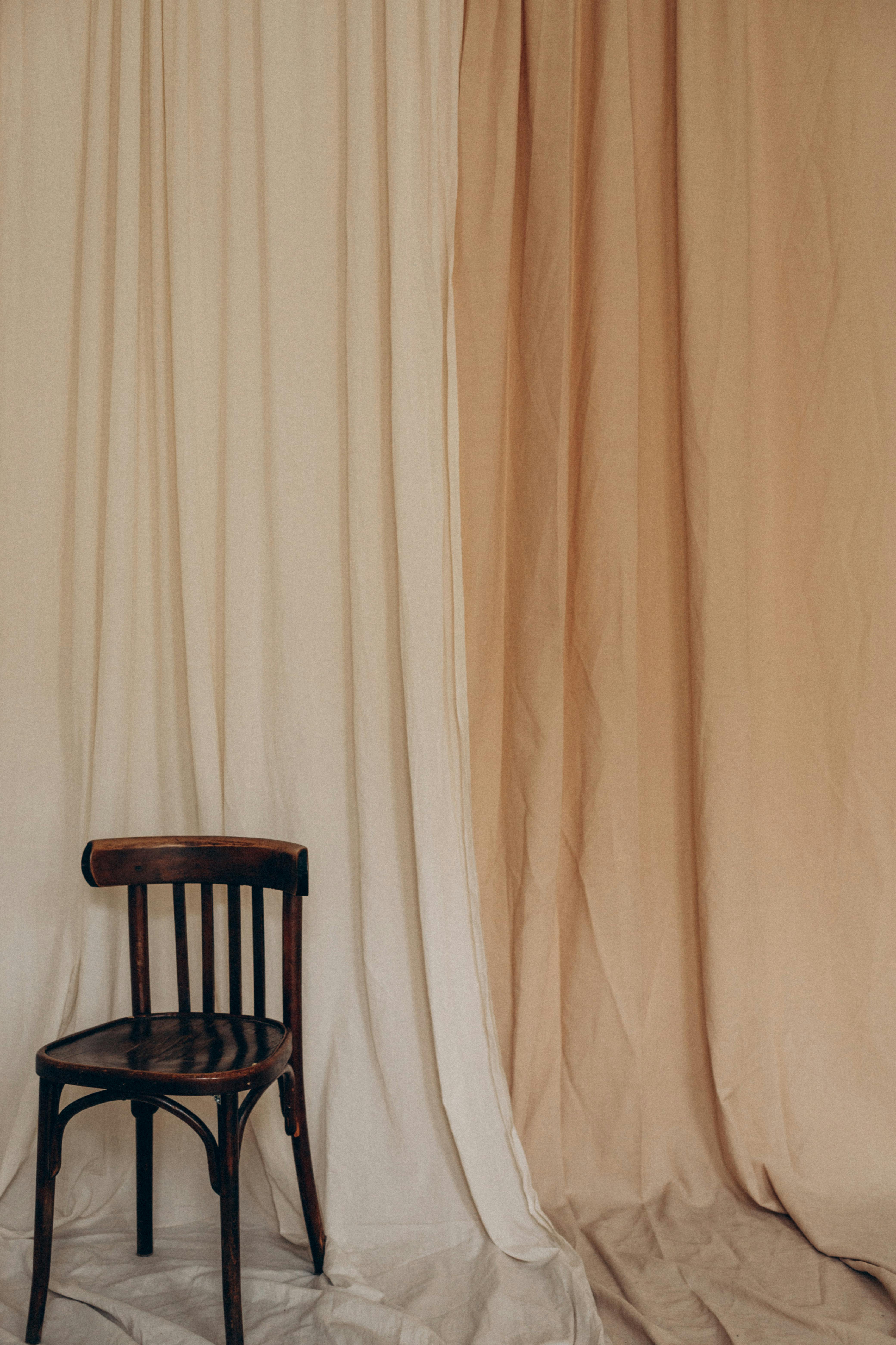 A classic wooden chair stands beside beige and cream curtains, creating a sophisticated vintage look.