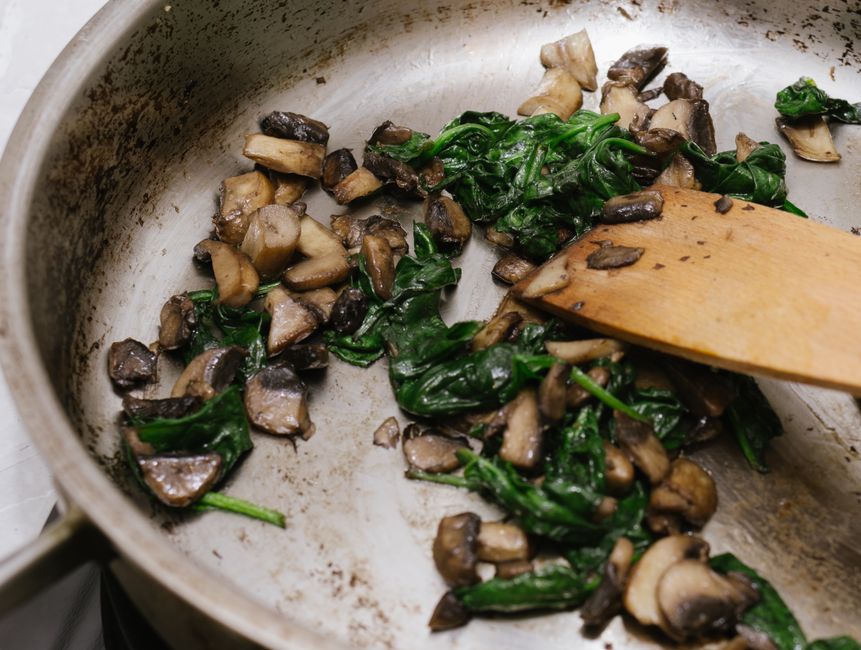 Close-up of mushrooms and spinach being sautéed in a frying pan.