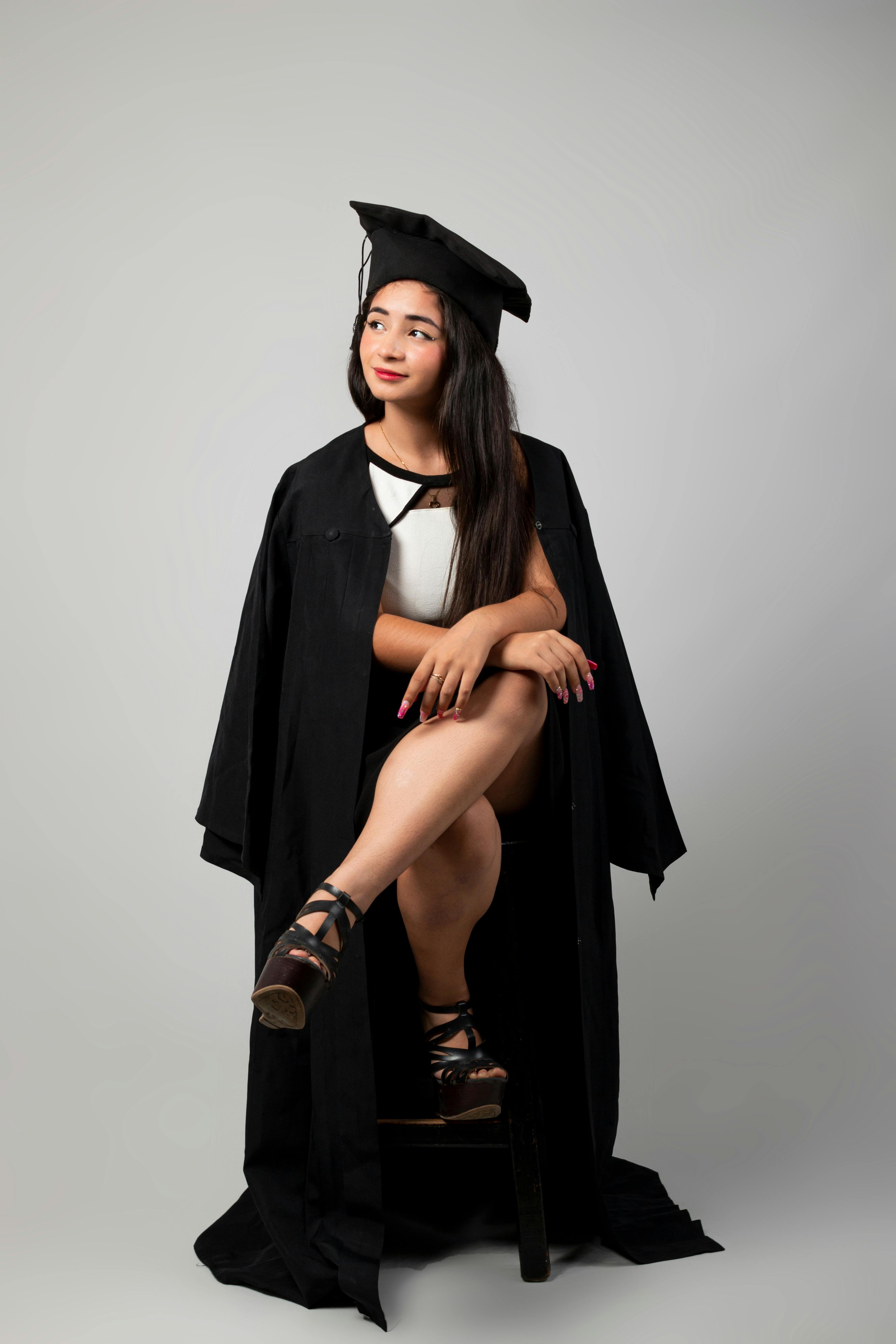 Portrait of a woman wearing a graduation gown and mortarboard, seated confidently in a studio.