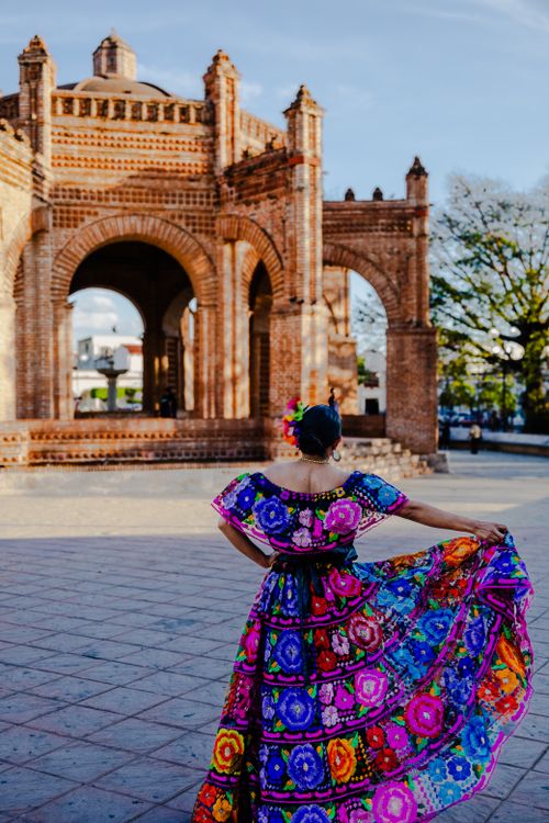 Free A vibrant woman in a traditional dress stands before La Pila fountain in Chiapa de Corzo's town square. Stock Photo