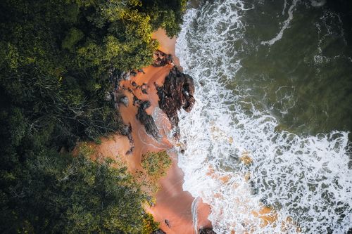 Free Dramatic aerial shot of a lush forest meeting the vibrant ocean waves at Chukai beach in Terengganu, Malaysia. Stock Photo